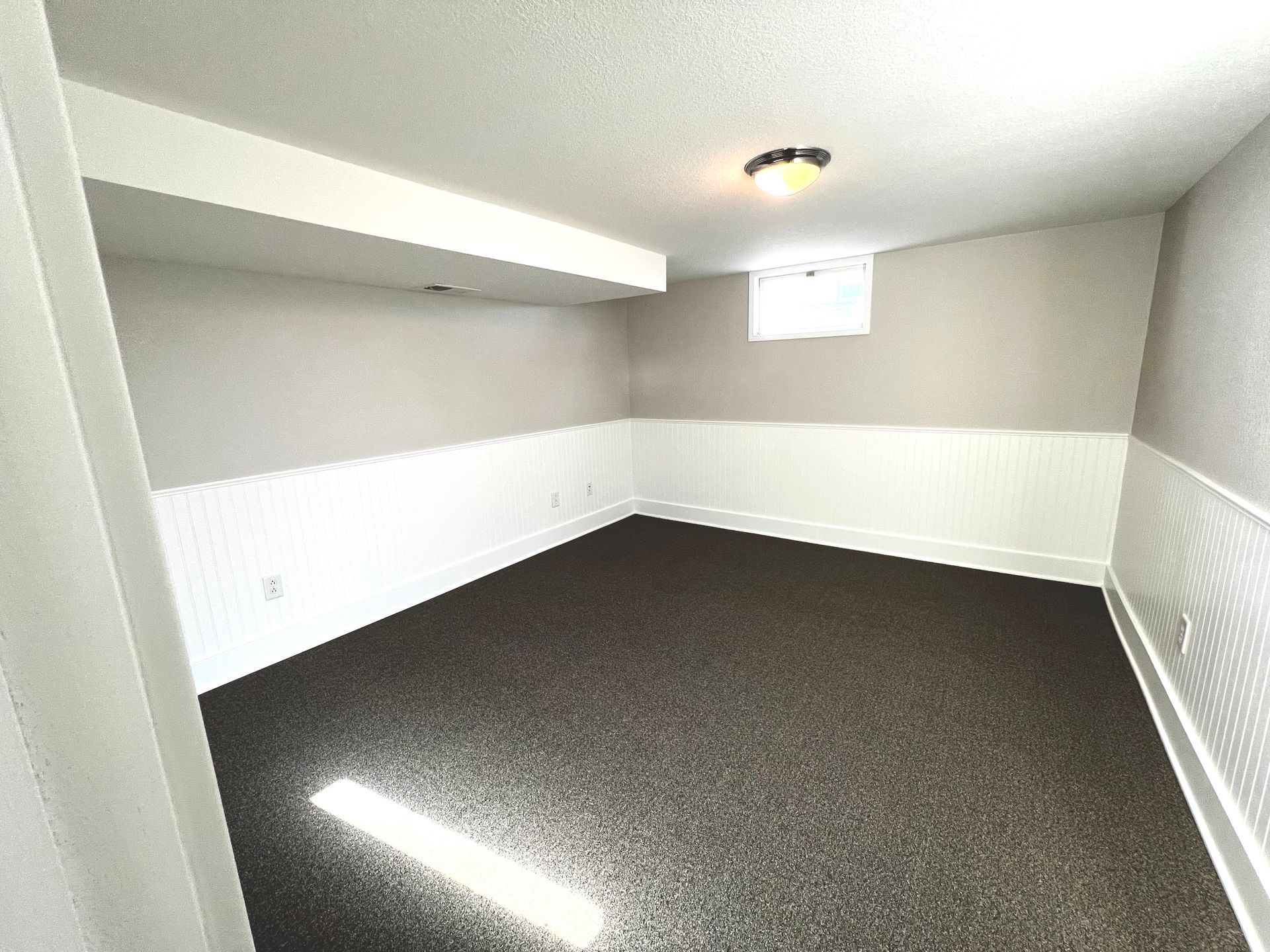 An empty basement with a carpeted floor and a window.