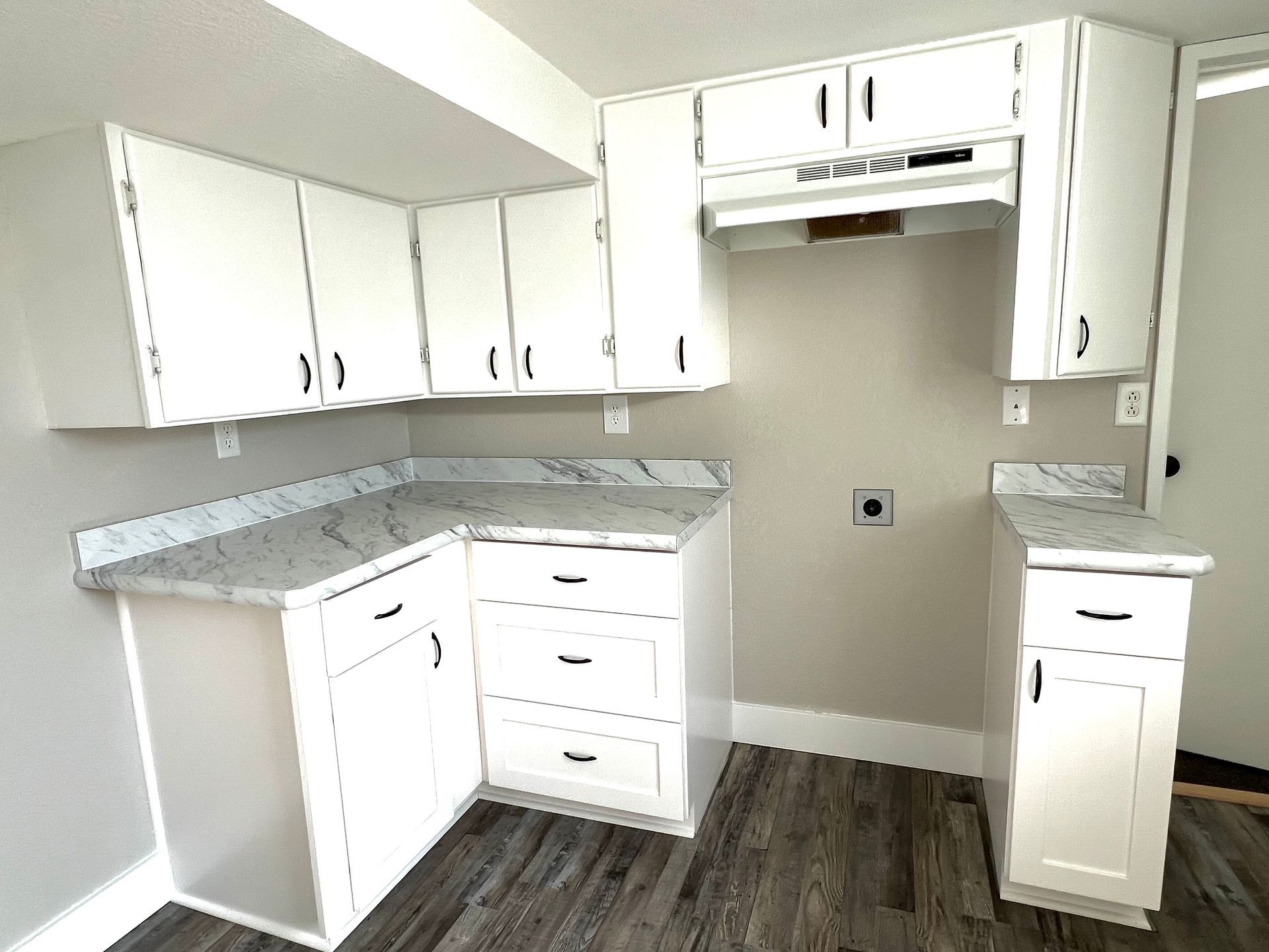 A kitchen with white cabinets and marble counter tops.