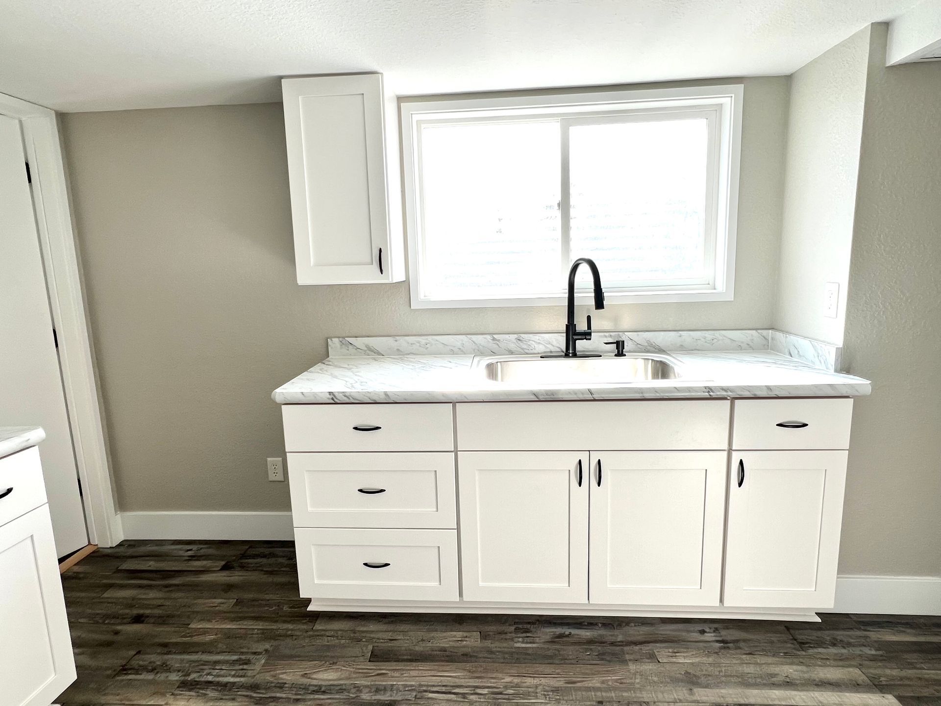 A kitchen with white cabinets , a sink , and a window.