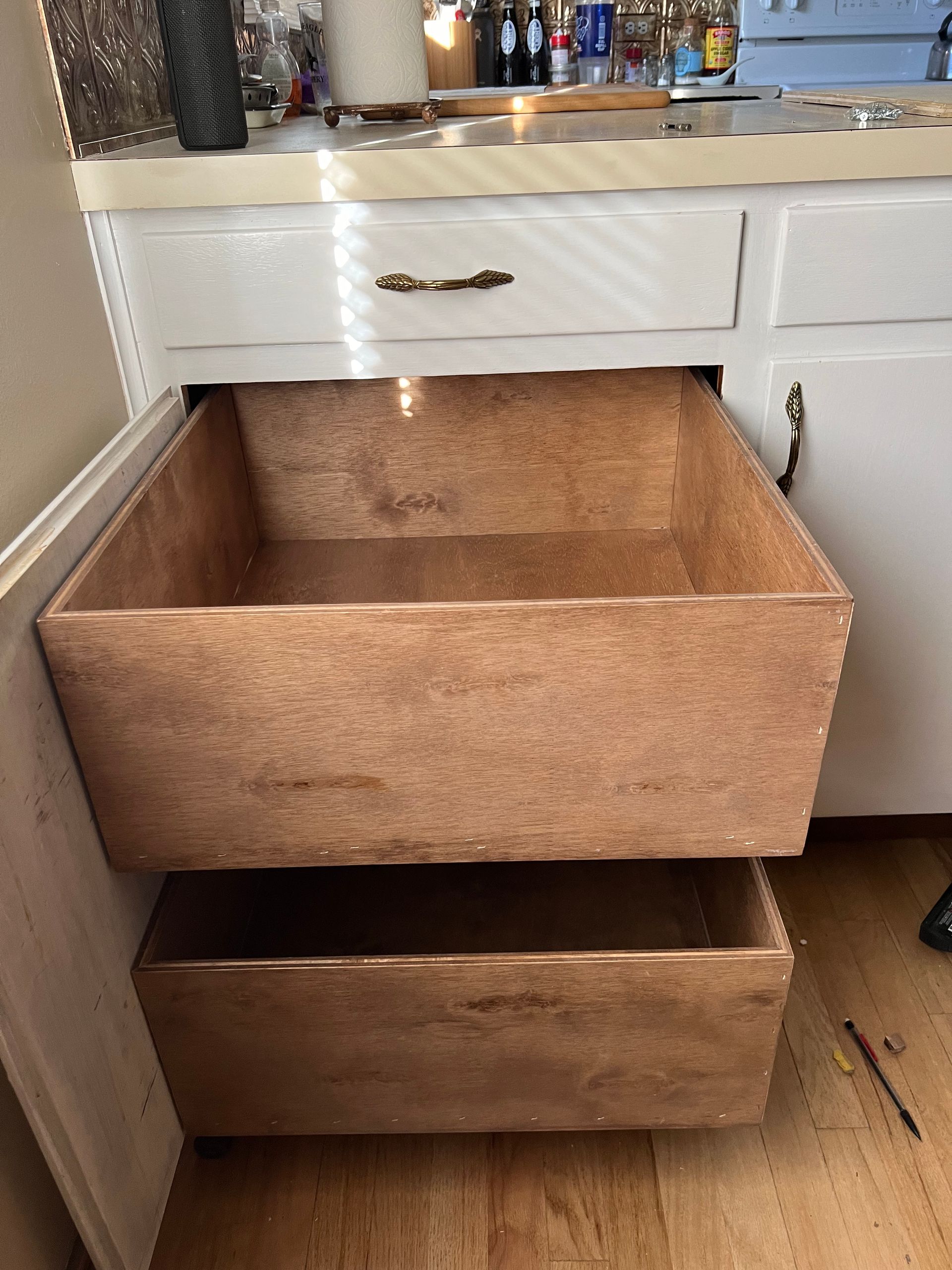 Two wooden drawers are open under a sink in a kitchen.