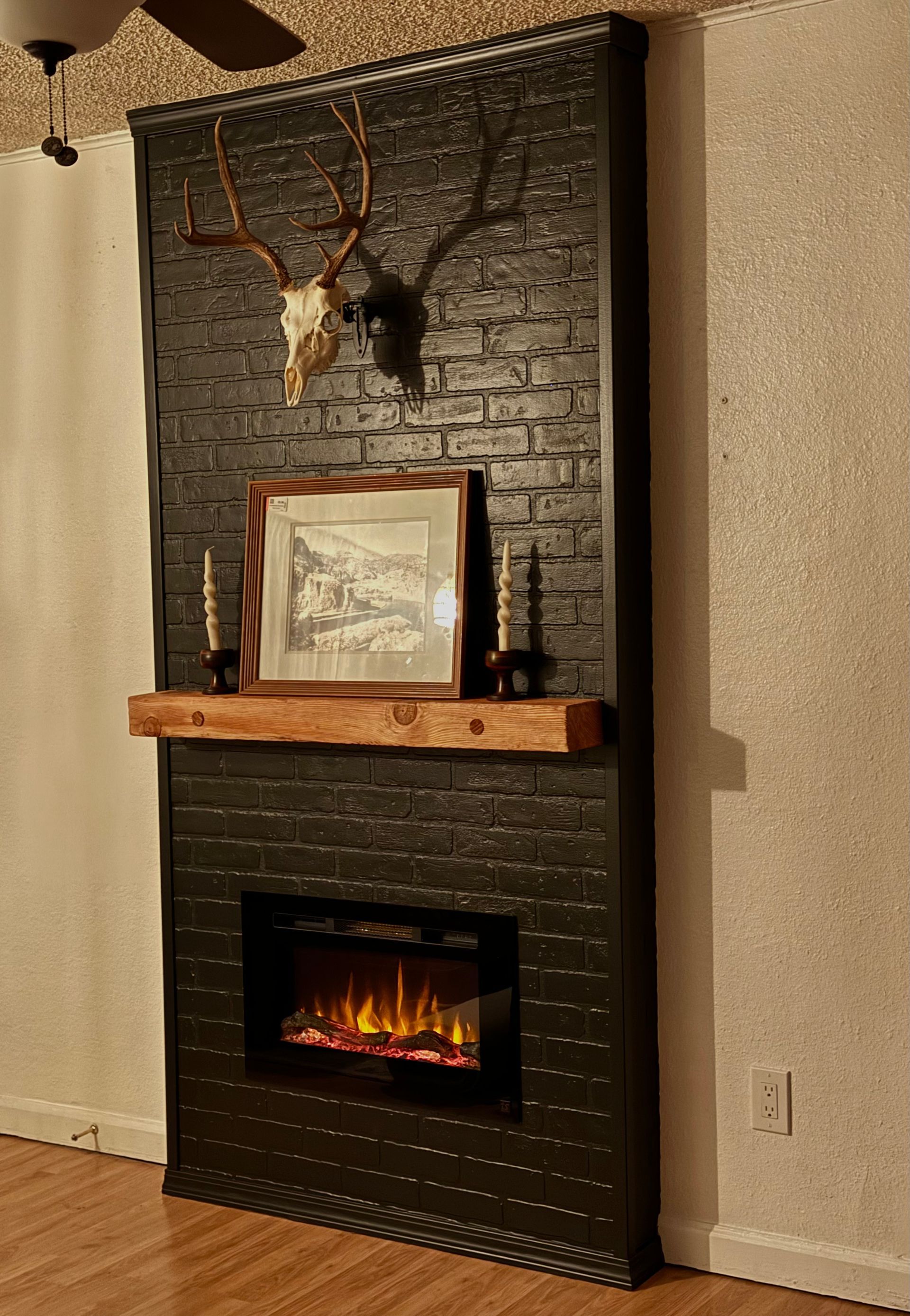 A fireplace with a picture on the mantle and a deer skull on the wall.
