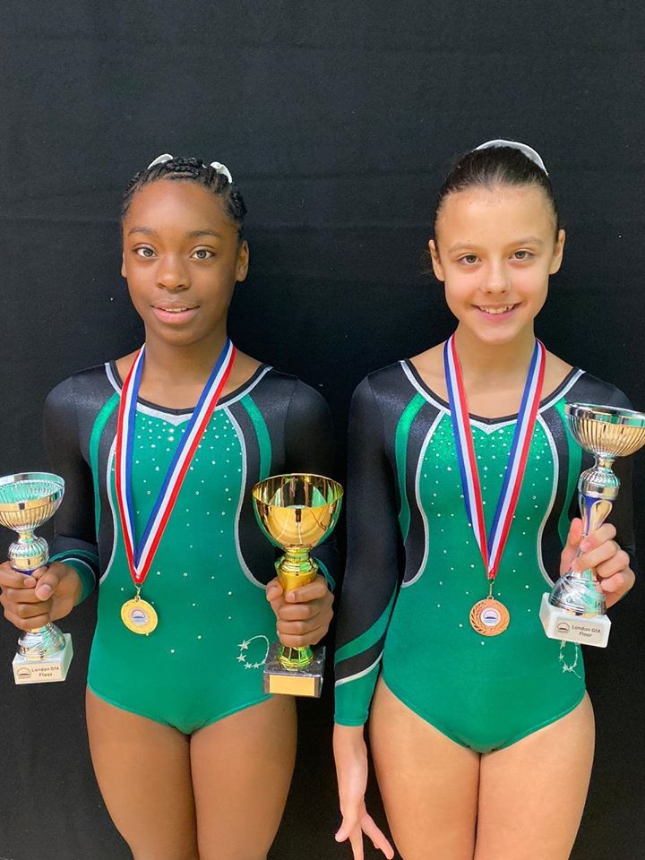 Gymnasts wearing medals and holding trophies, smiling and celebrating after a competition