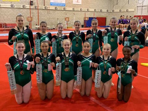 Large group of gymnasts with medals and ribbons smiling after their competition