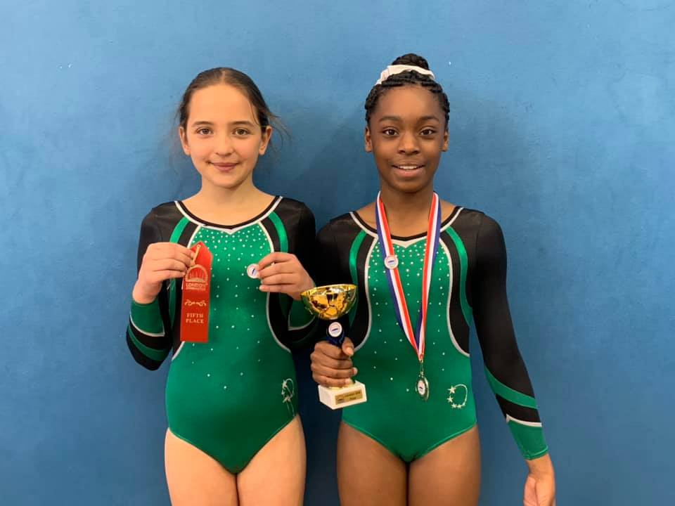 Gymnasts wearing medals and holding a trophy smiling after a competition