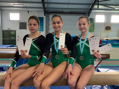 Gymnasts with medals sat on a beam smiling after their competition