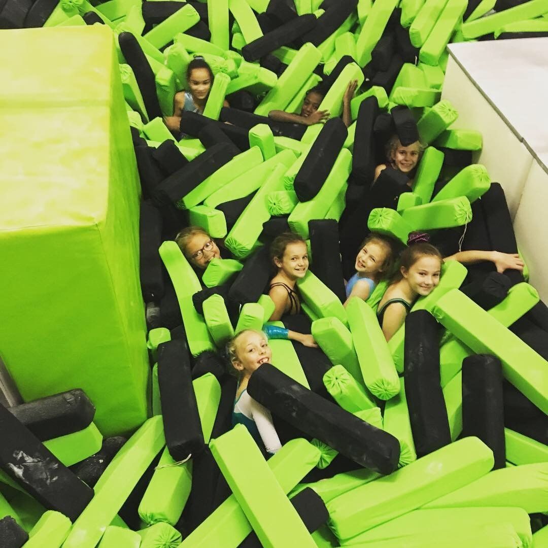 Join Our Club! A group of gymnasts having fun sitting in a foam pit together