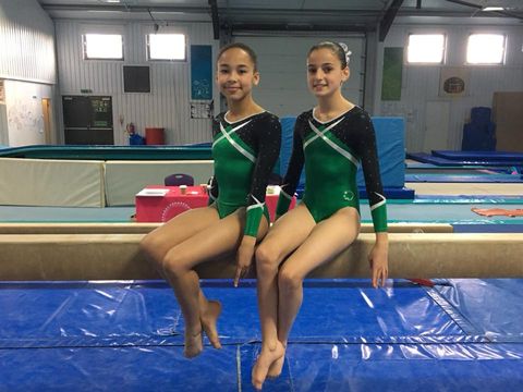 Gymnasts sitting on a beam after competing at the twin piece competition
