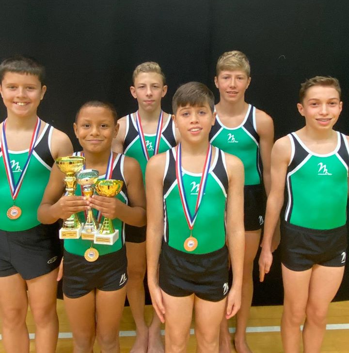 Gymnasts wearing medals and holding trophies, smiling and celebrating after a competition