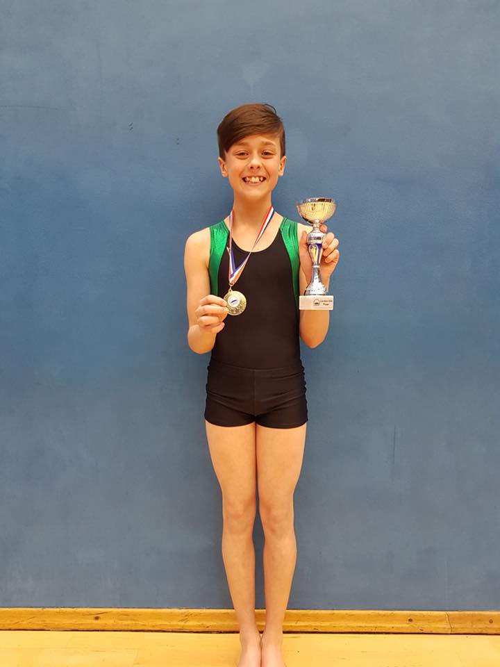 Male gymnast with a medal, trophy and an achievement pin