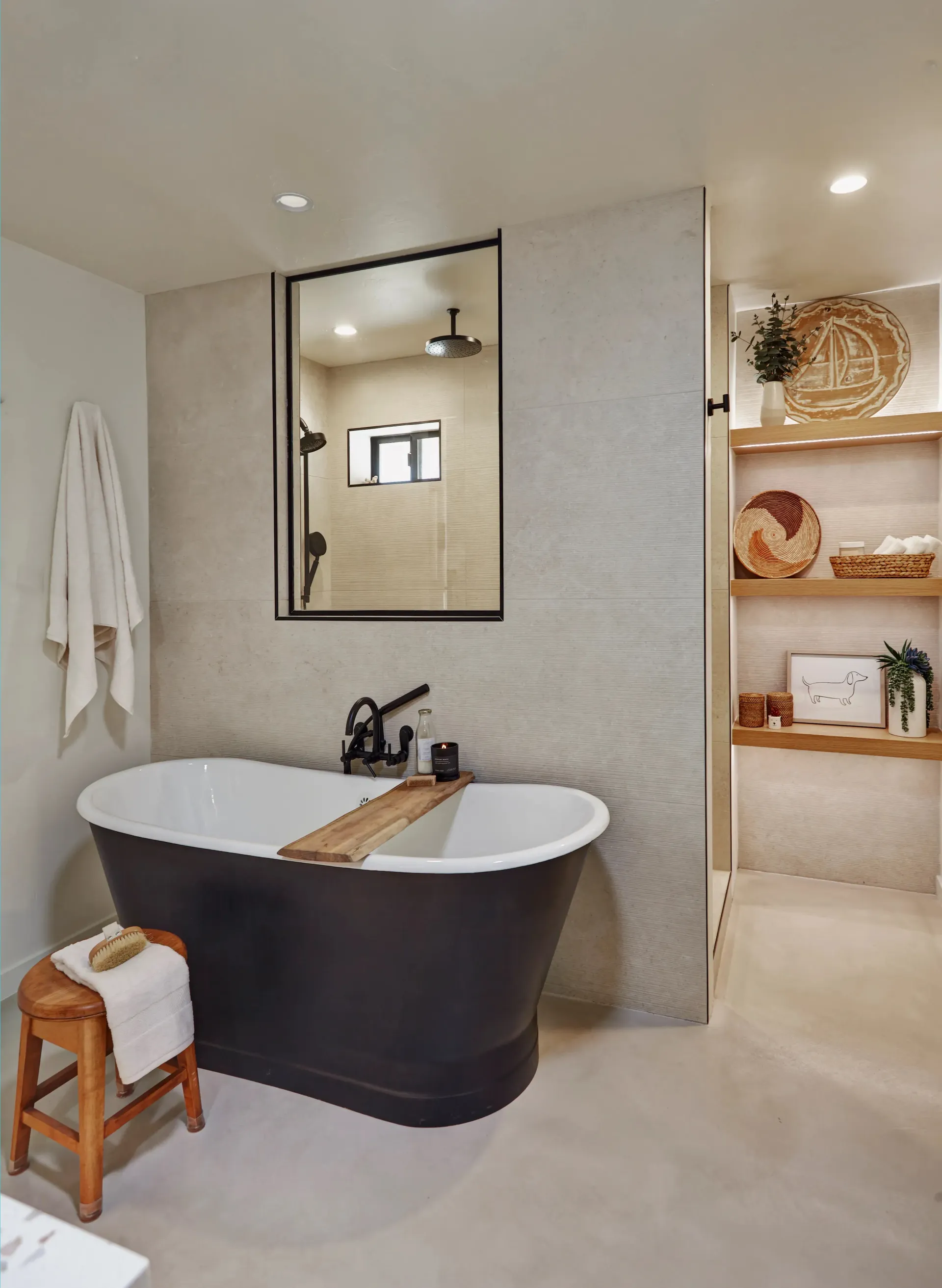 Bathroom with a black freestanding tub, neutral tile, and open shower view. Wooden shelves with decor.