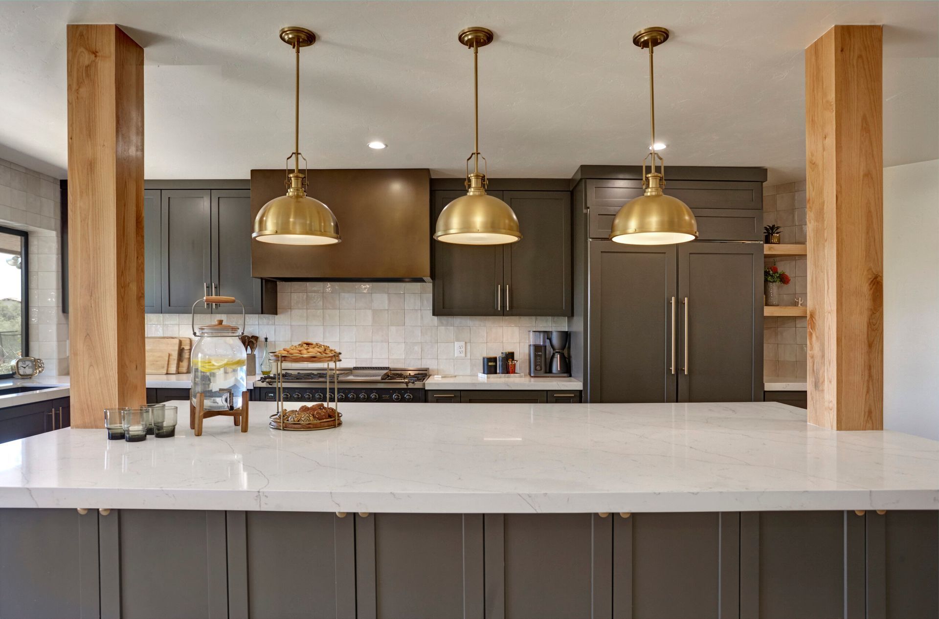 Kitchen with gold pendant lights over a white countertop island, gray cabinets, and wooden posts.