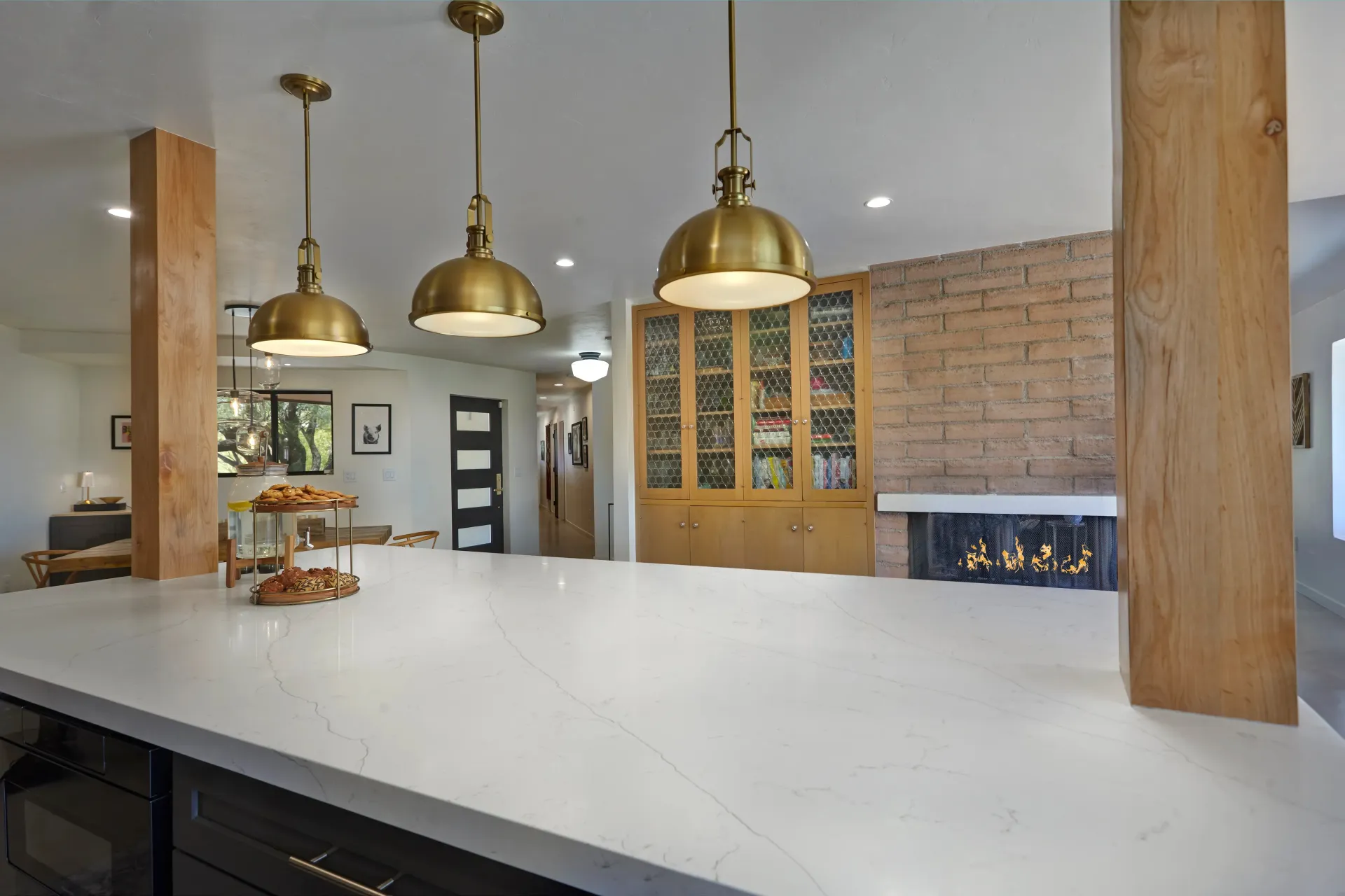 Modern kitchen with white countertop, brass pendant lights, and brick fireplace.