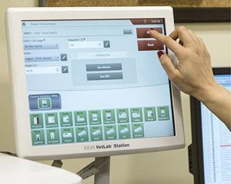Hand reaching toward a touchscreen monitor with a medical interface and green control buttons