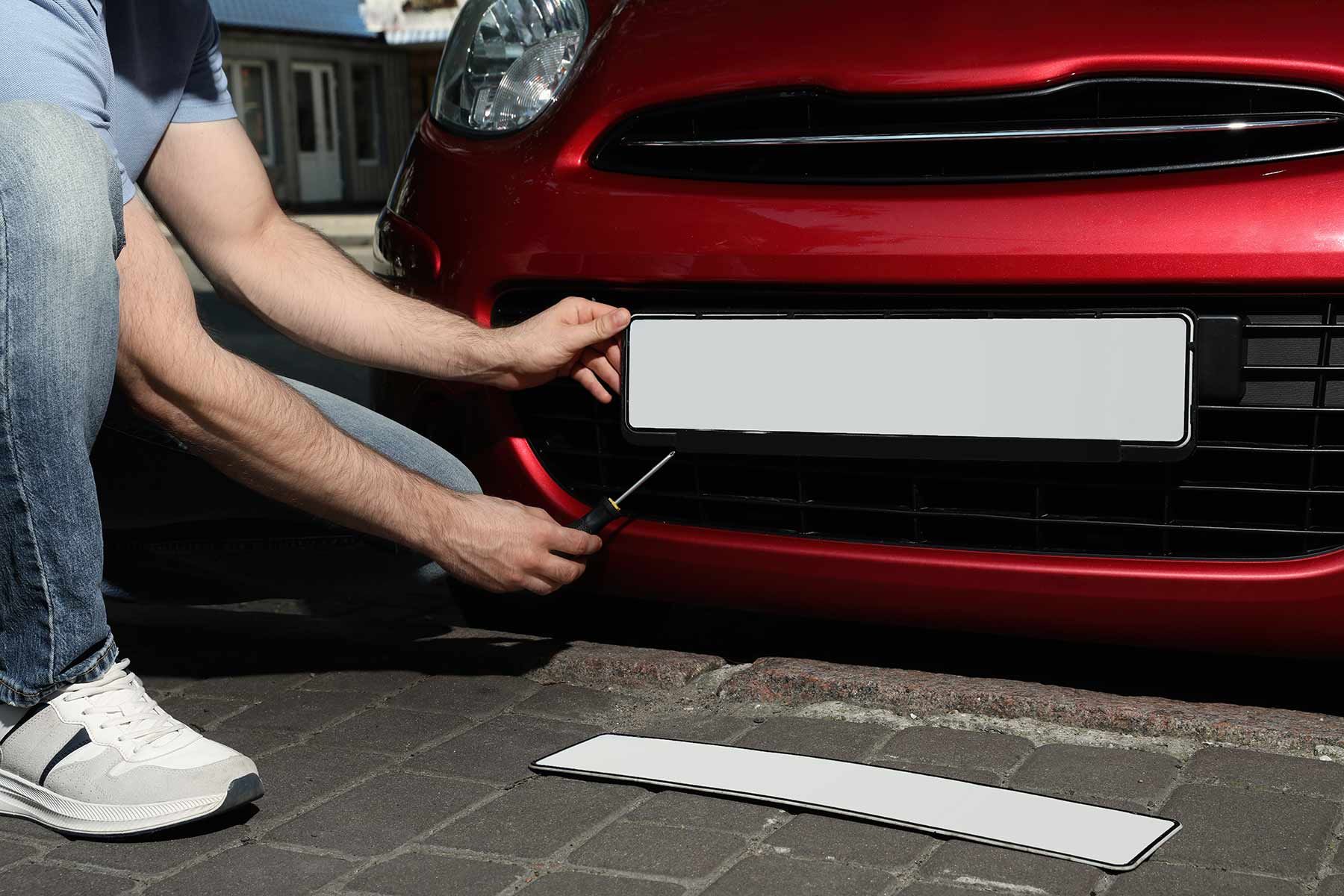 A Man is Putting a License Plate on a red car — Auto Marvel In Mount Saint John, QLD