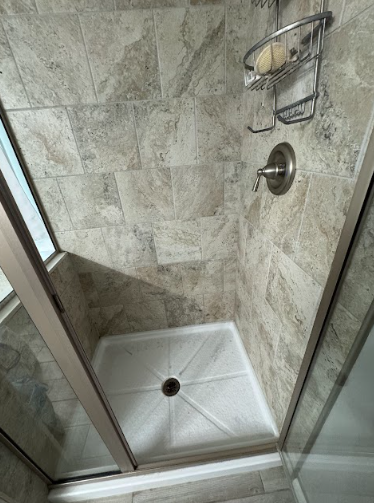 A small, tiled shower with a white base, glass doors, and a soap holder.