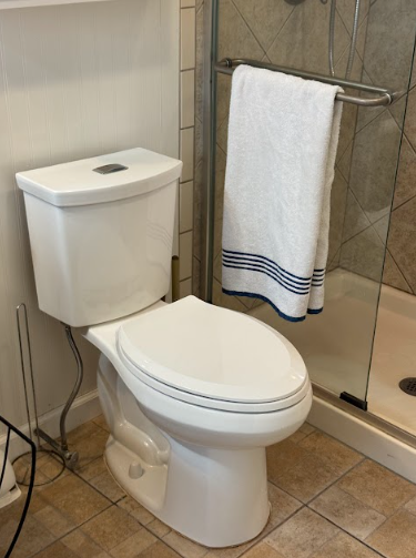 White toilet in a bathroom. A white towel with blue stripes hangs on a glass shower door in the background.