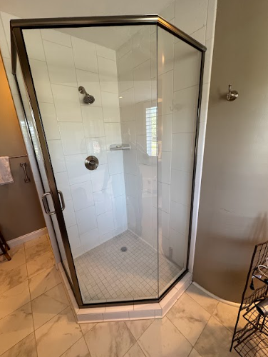 A corner shower with a dark-framed glass enclosure, white tiled walls, and a gray and white tiled floor.