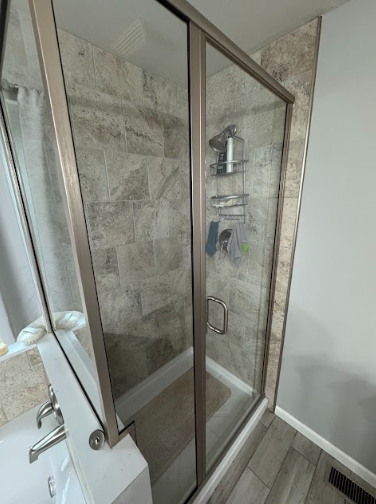 Shower stall with a glass door and tiled walls, next to a bathtub. Gray and tan tones.