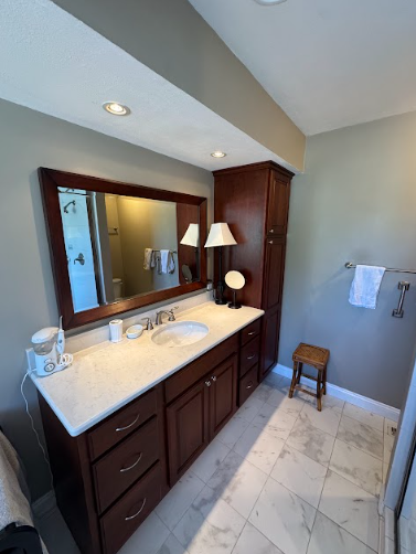 Bathroom with a dark wood vanity, large mirror, and marble-look tile floor. A towel rack and small stool are visible.