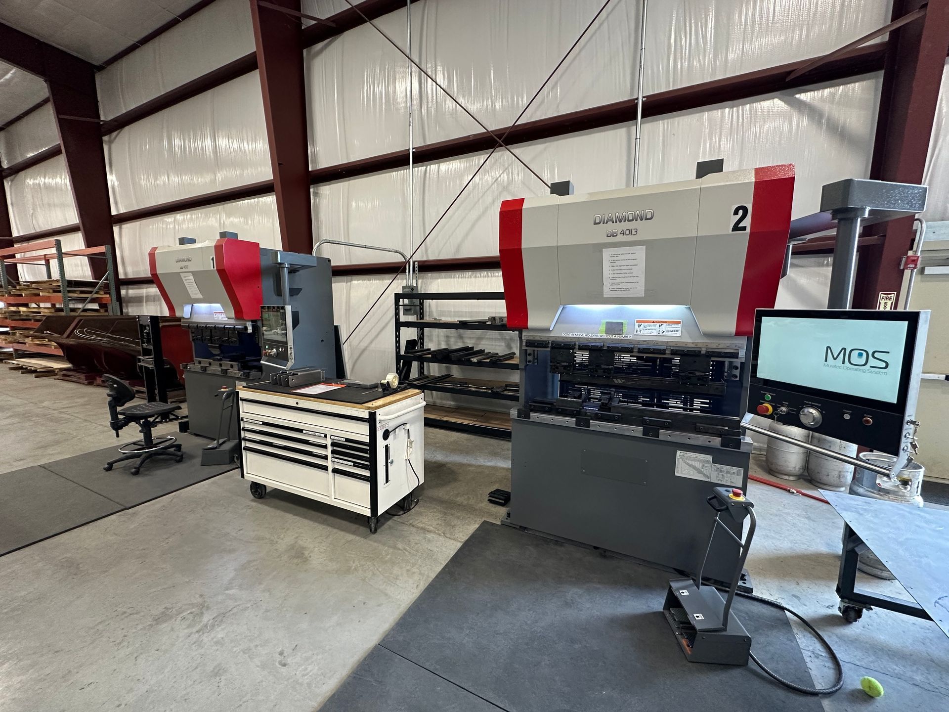 Manufacturing equipment in an industrial setting: press brakes, control panels, a toolbox, and shelving.