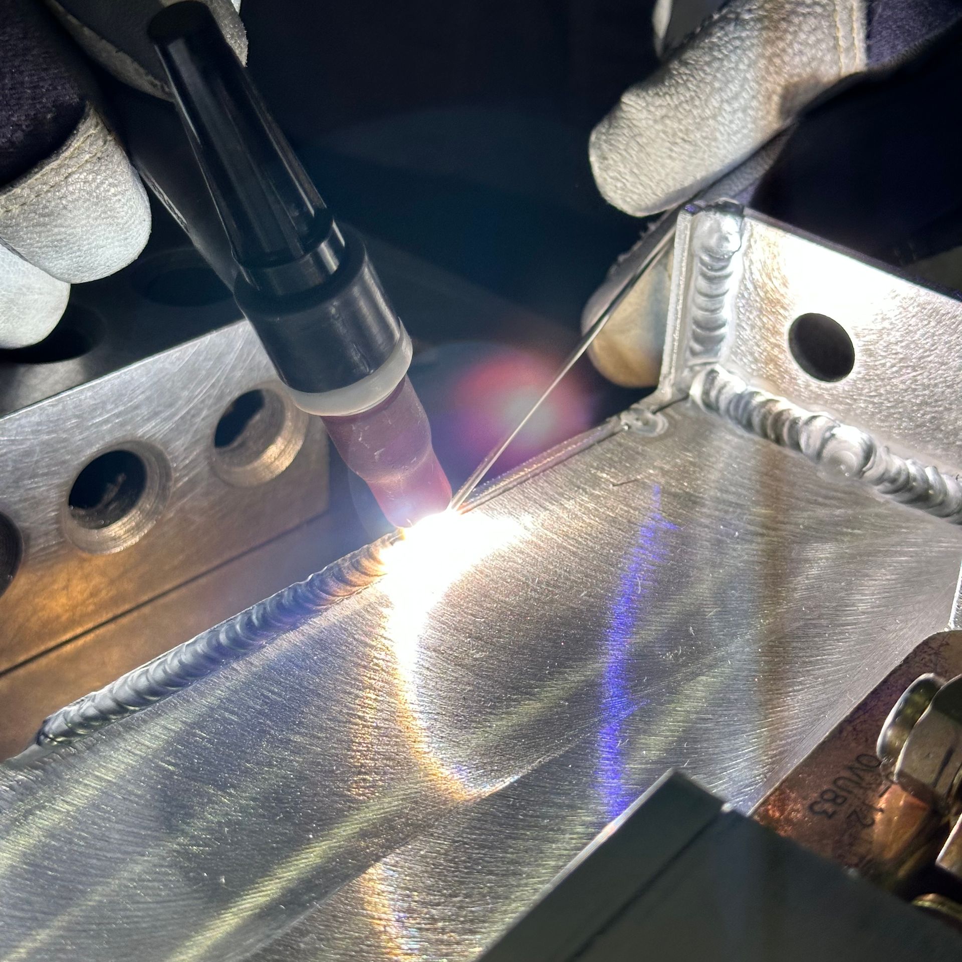 A person welding metal corners with bright light and protective gloves.