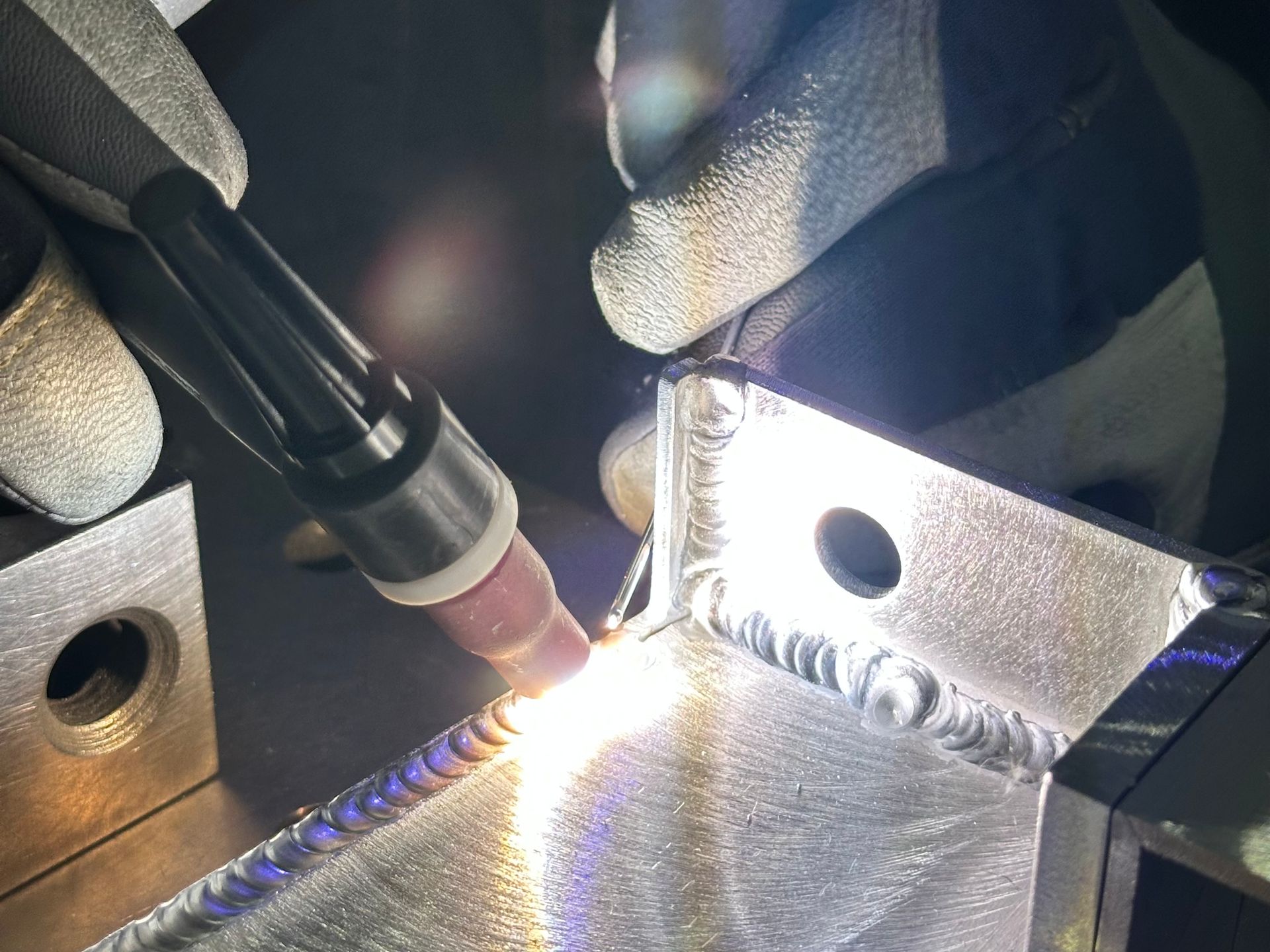 Welder using a torch on metal, creating sparks and a weld. Hands wearing gloves.
