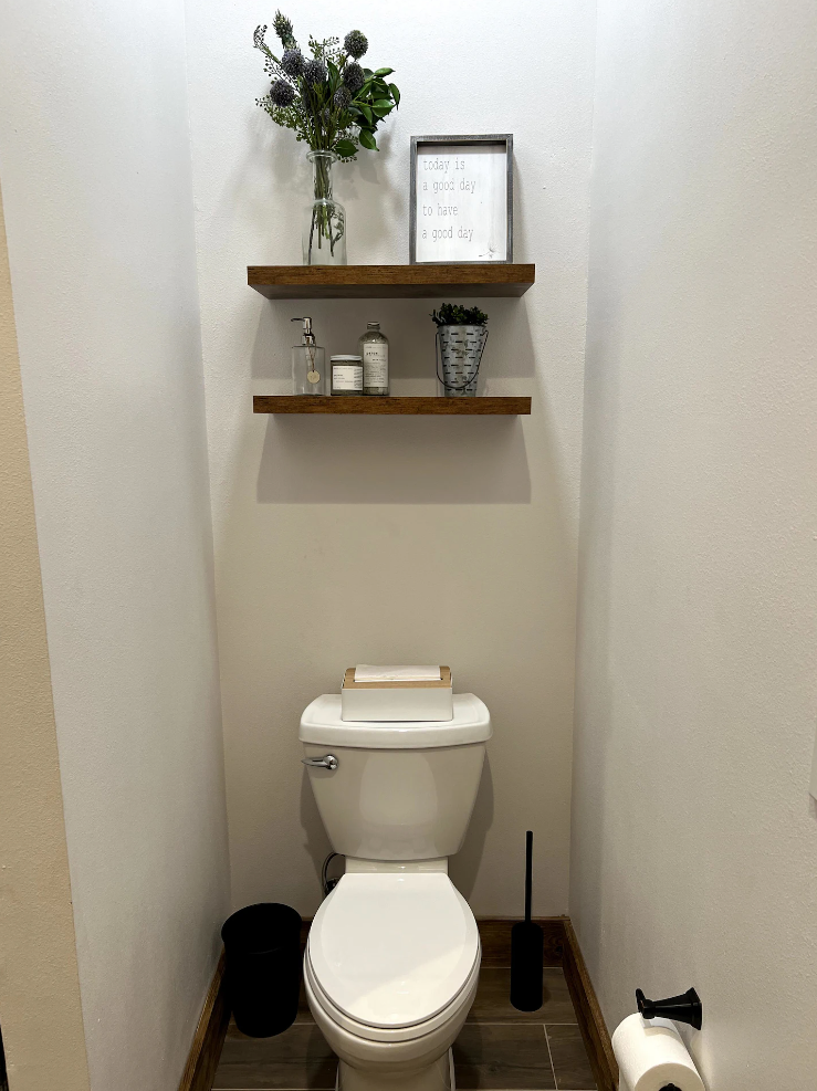 A toilet in a small bathroom with two shelves above it.