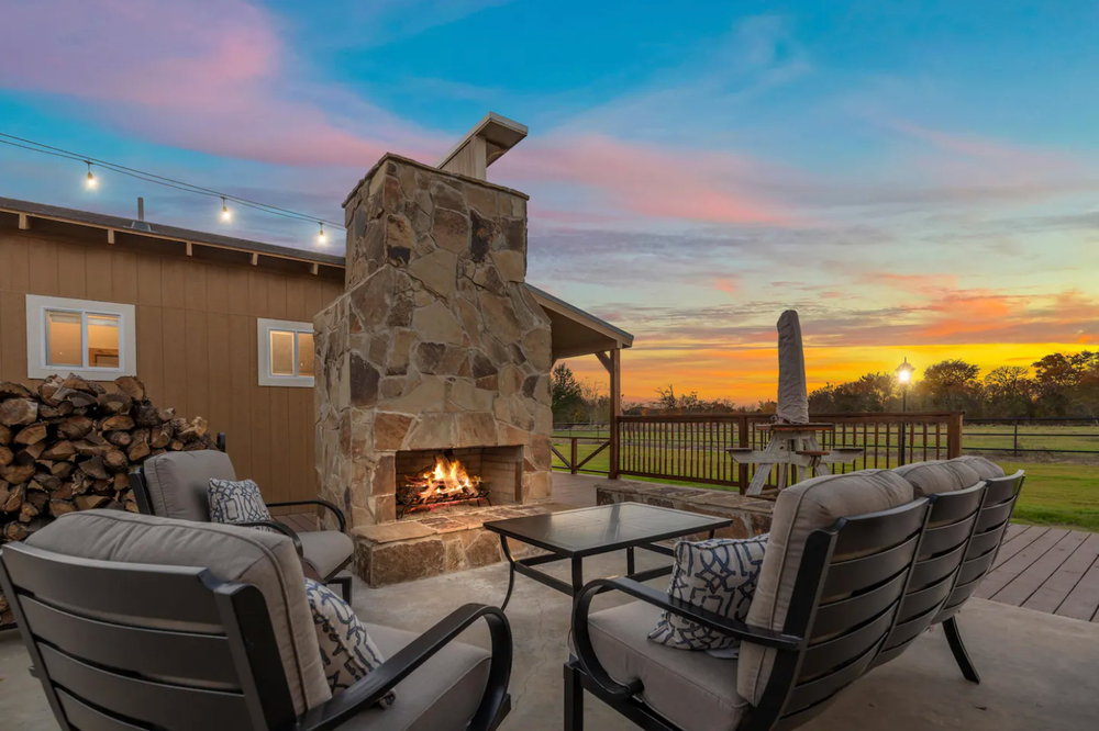 A patio with a fireplace and chairs at sunset.