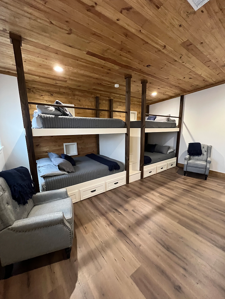 A room with bunk beds , chairs , and a wooden ceiling.
