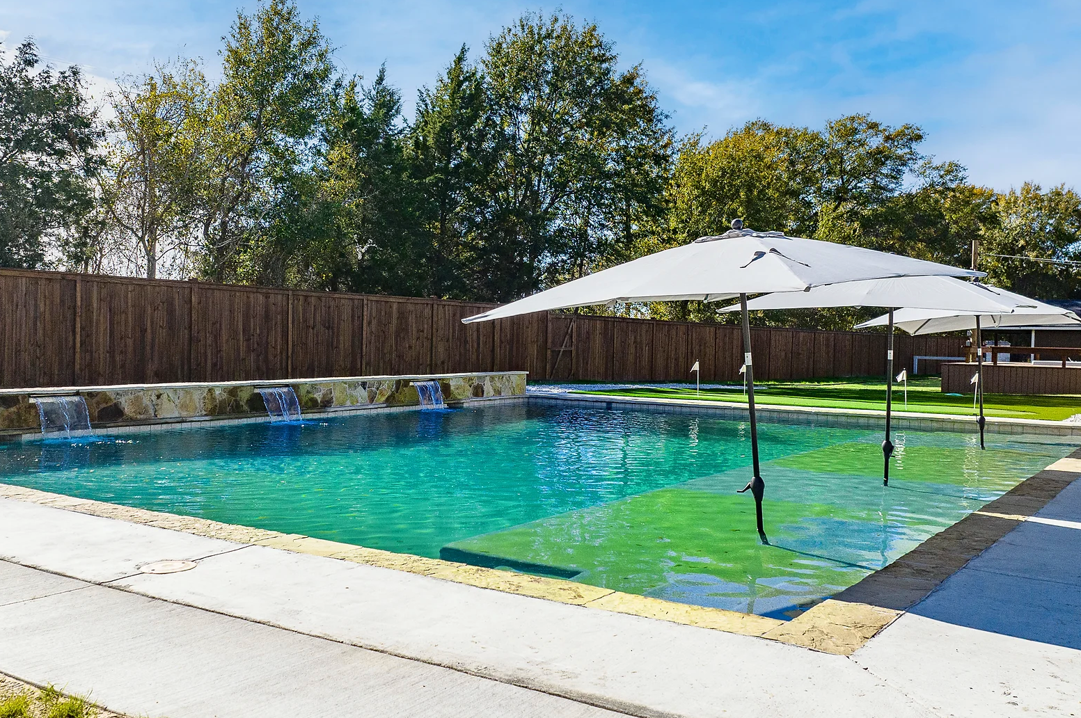 A large swimming pool surrounded by umbrellas and a wooden fence.