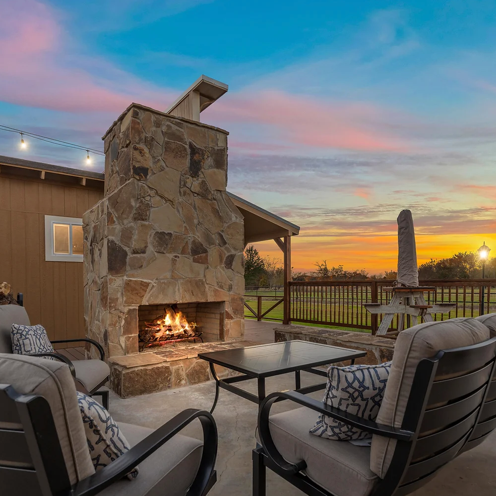 A patio with a fireplace and chairs at sunset