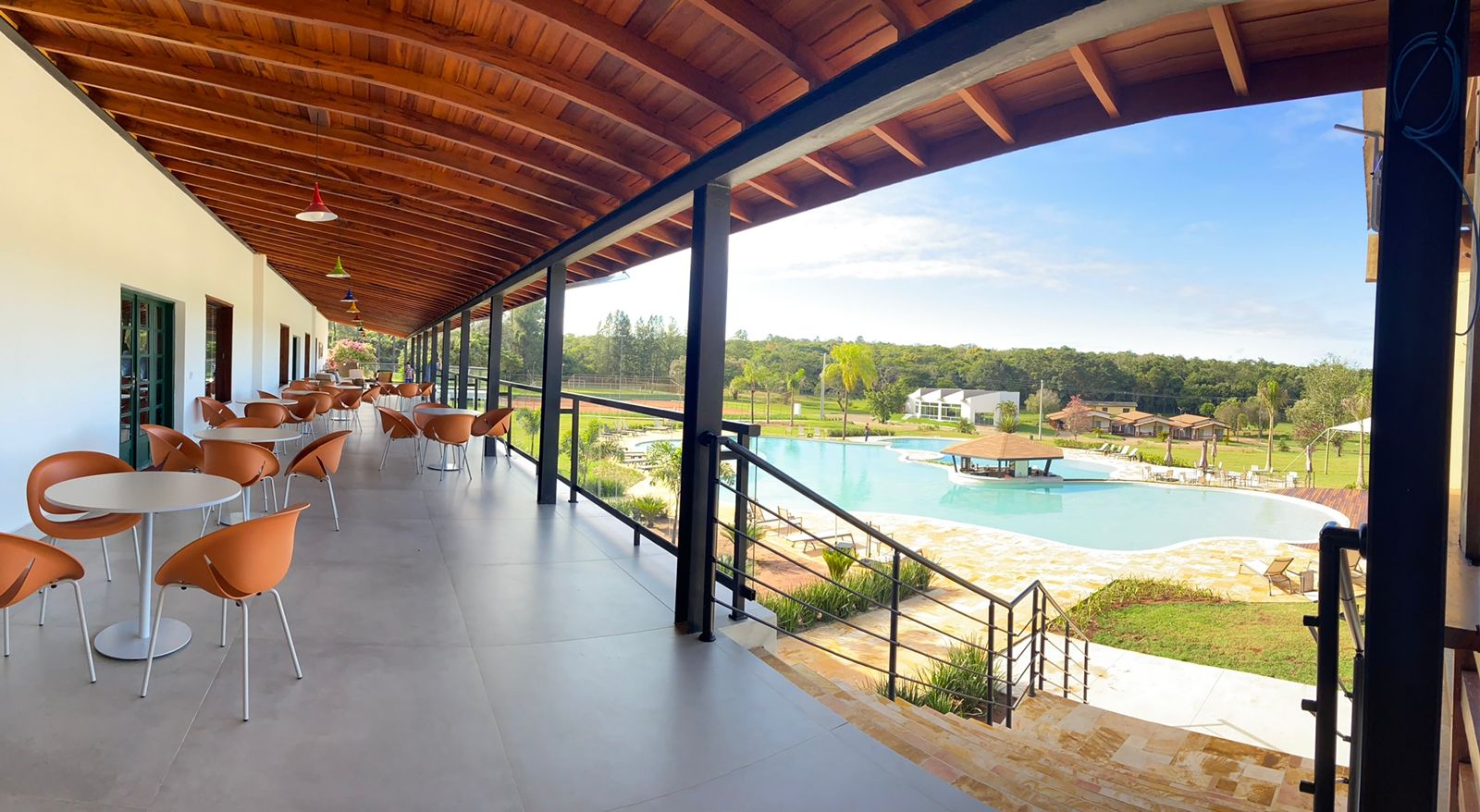 Uma grande varanda com mesas e cadeiras com vista para a piscina.