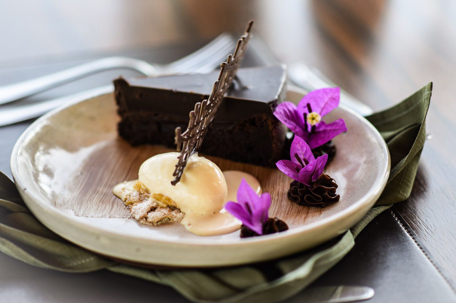 Um prato branco coberto com um pedaço de bolo de chocolate e flores roxas.