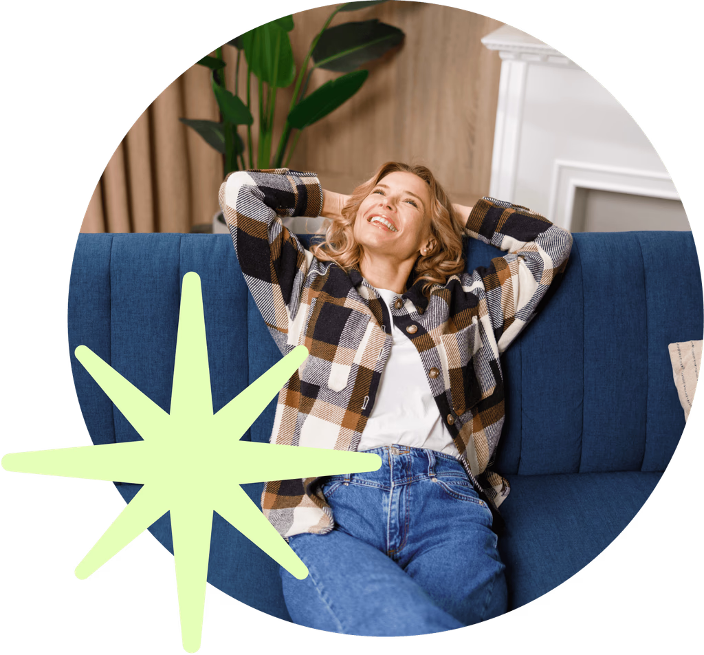 A woman is sitting on a blue couch with her hands behind her head.