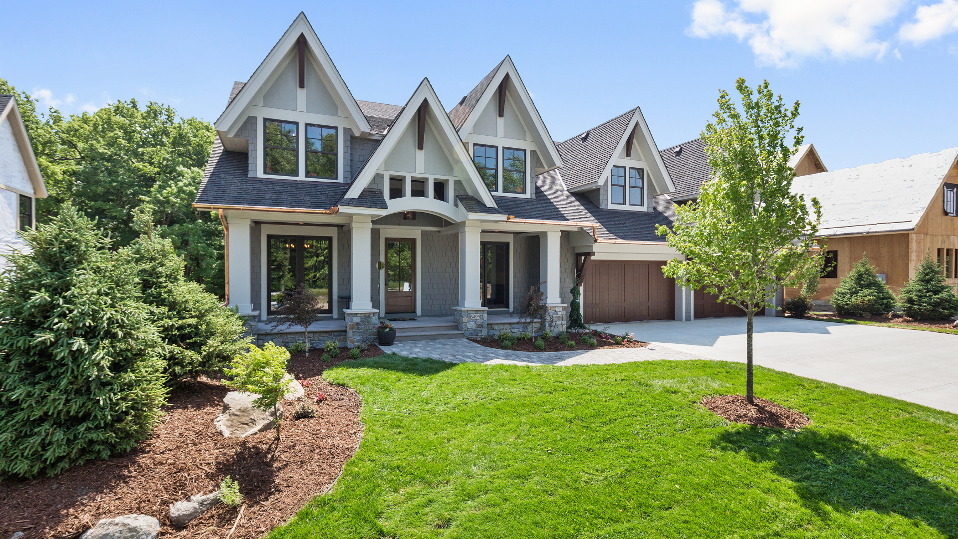 Gray house with multiple gables, stone porch, and garage. Green lawn and trees surround the home.