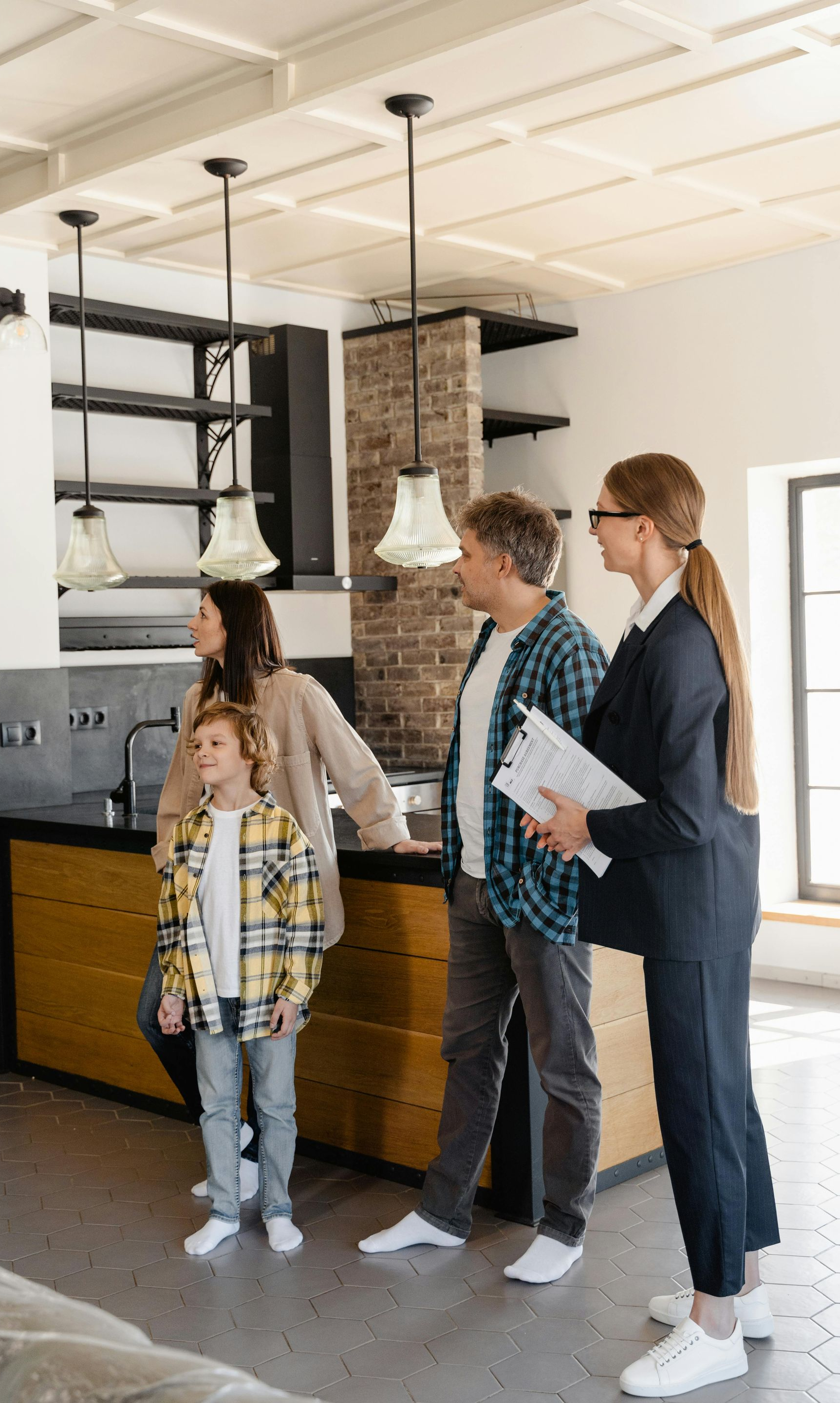 Family and realtor viewing a kitchen. The realtor holds papers; the family looks around.