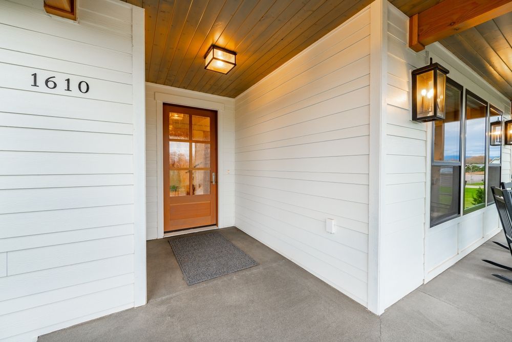 The front porch of a house with a brown door and white siding.