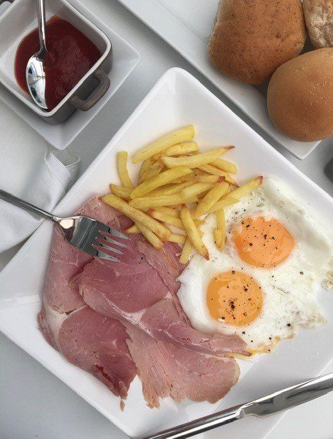 A white plate topped with ham eggs and french fries
