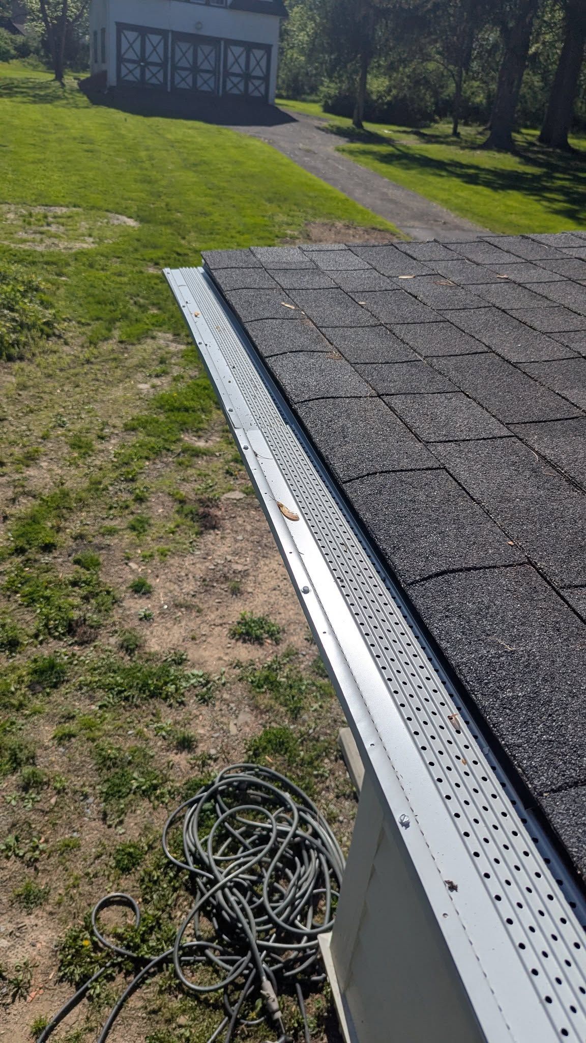 A close up of a gutter on a roof with a house in the background.