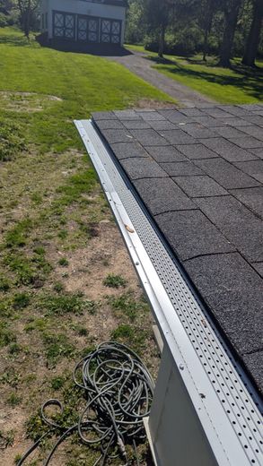 A close up of a gutter on a roof with a house in the background.