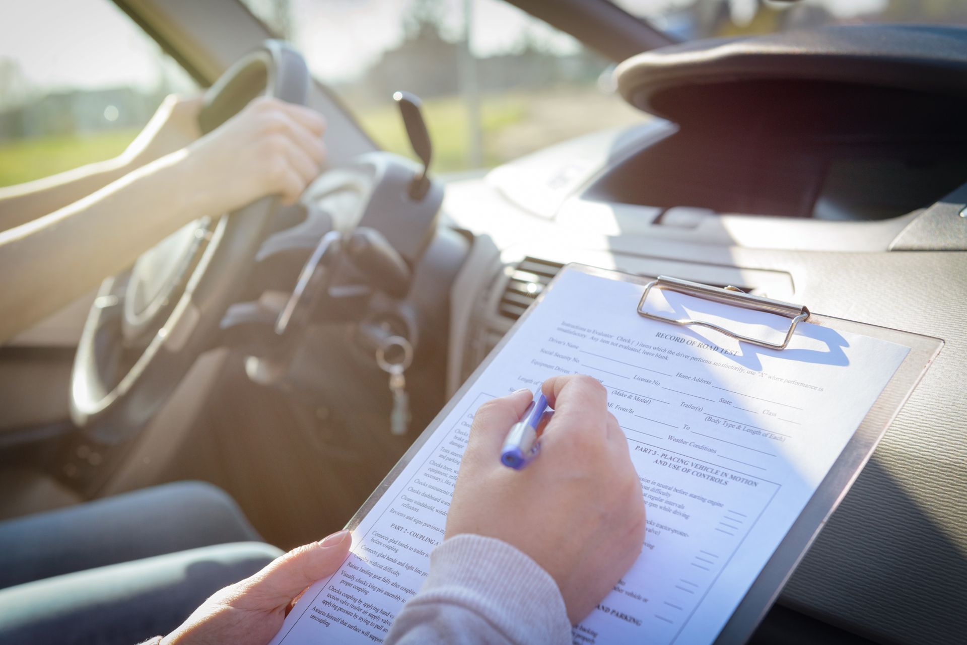 A person is sitting in a car writing on a clipboard