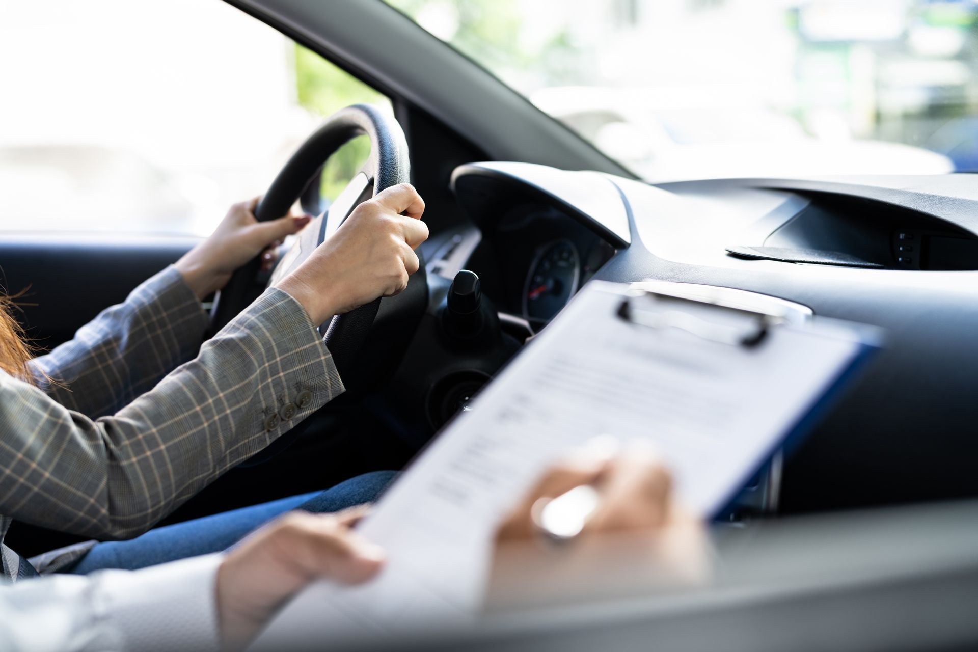 A woman is driving a car and holding a clipboard