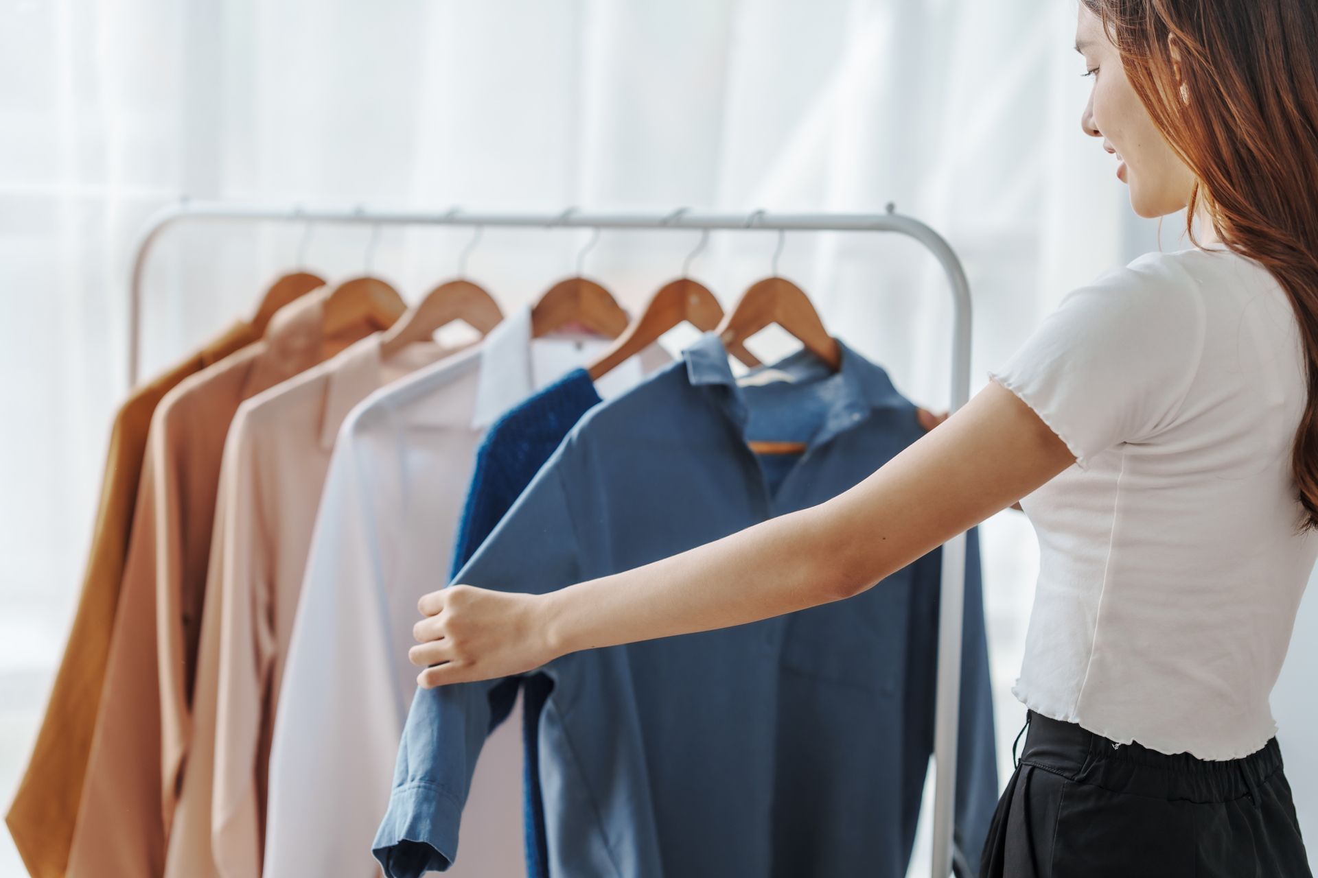A woman is holding a shirt in front of a rack of clothes