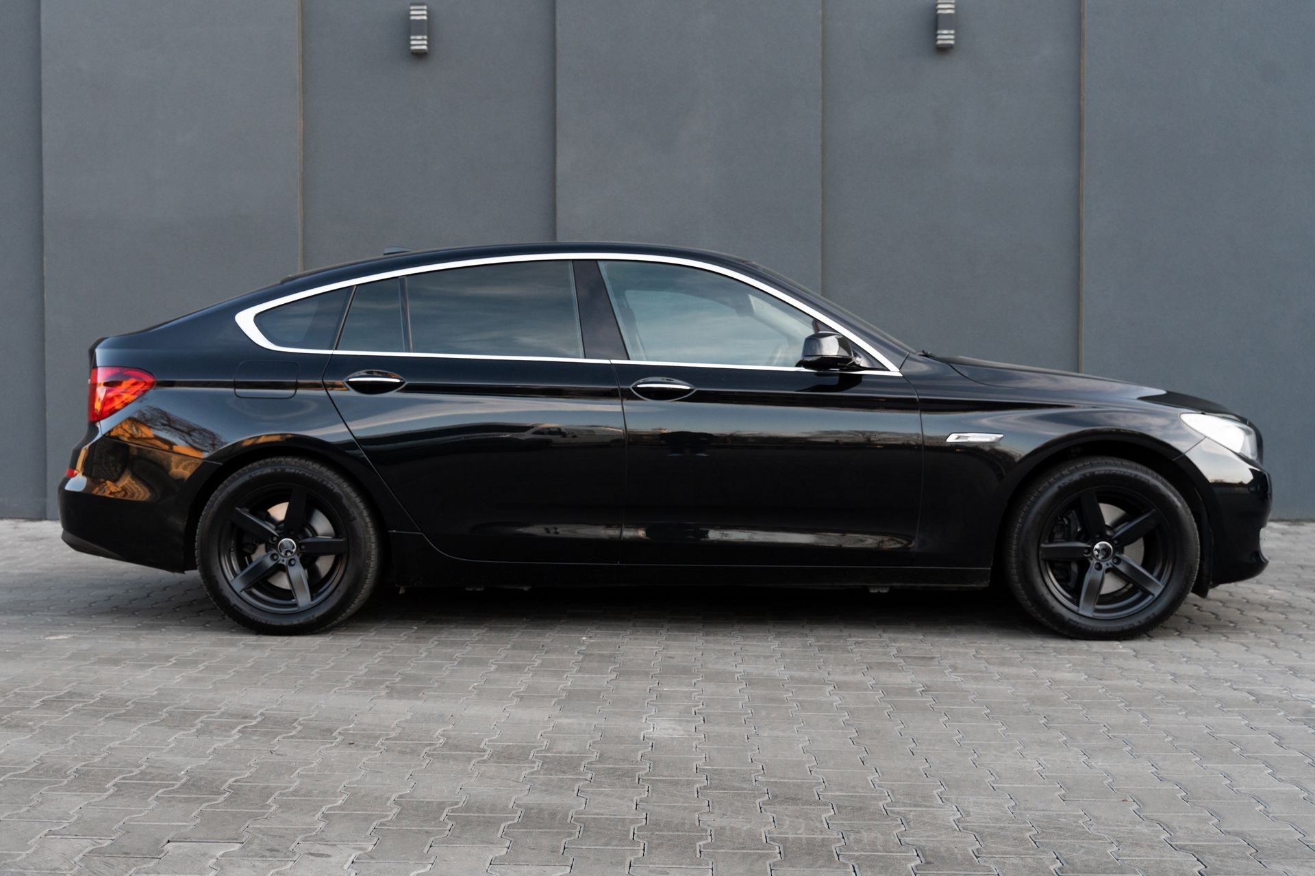 A black car is parked in front of a gray wall