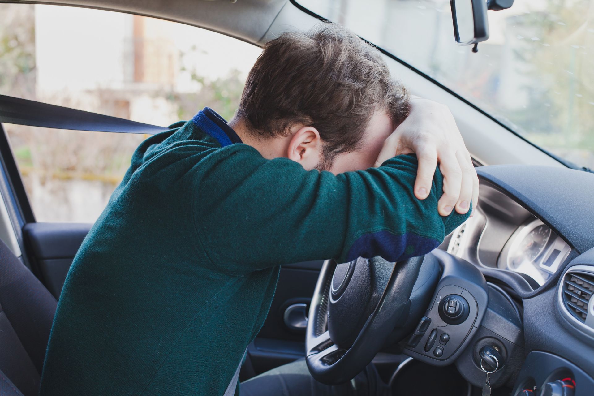 A man is sitting in a car with his head on the steering wheel