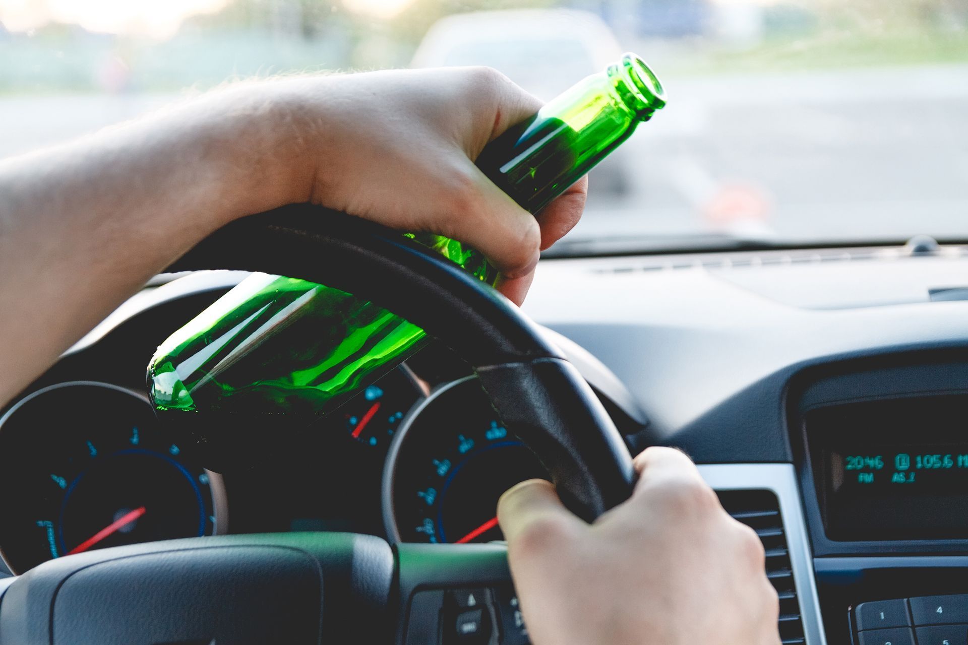 A person is holding a bottle of beer while driving a car