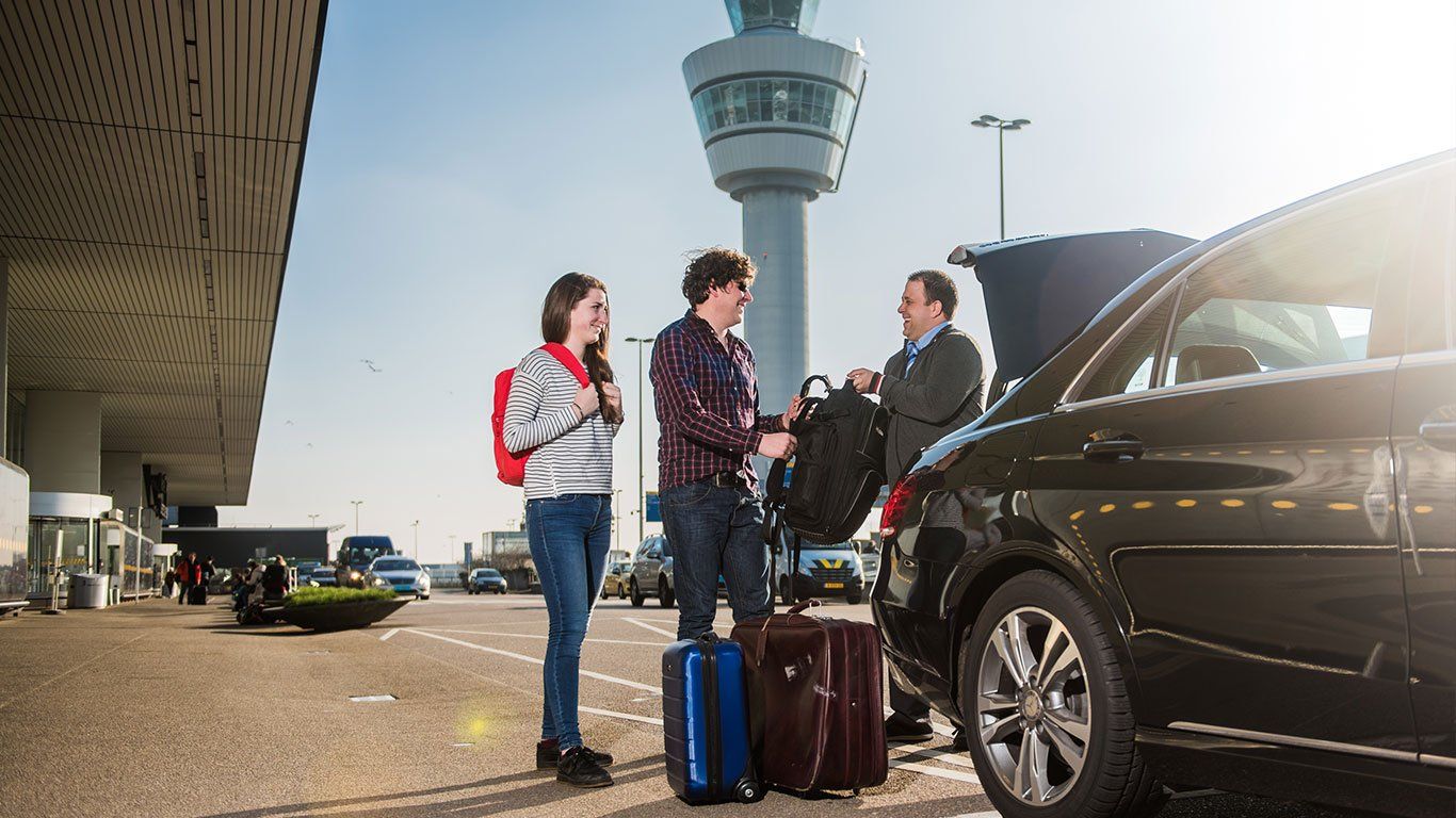 Een groep mensen staat naast een auto op een luchthaven.