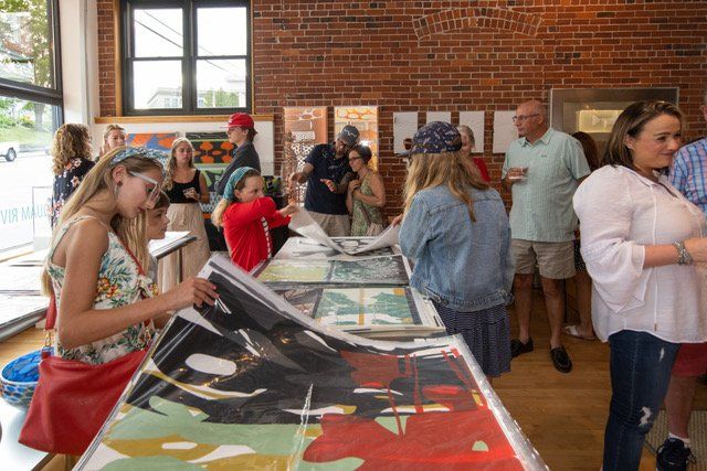 A group of people are looking at paintings in a room with a brick wall