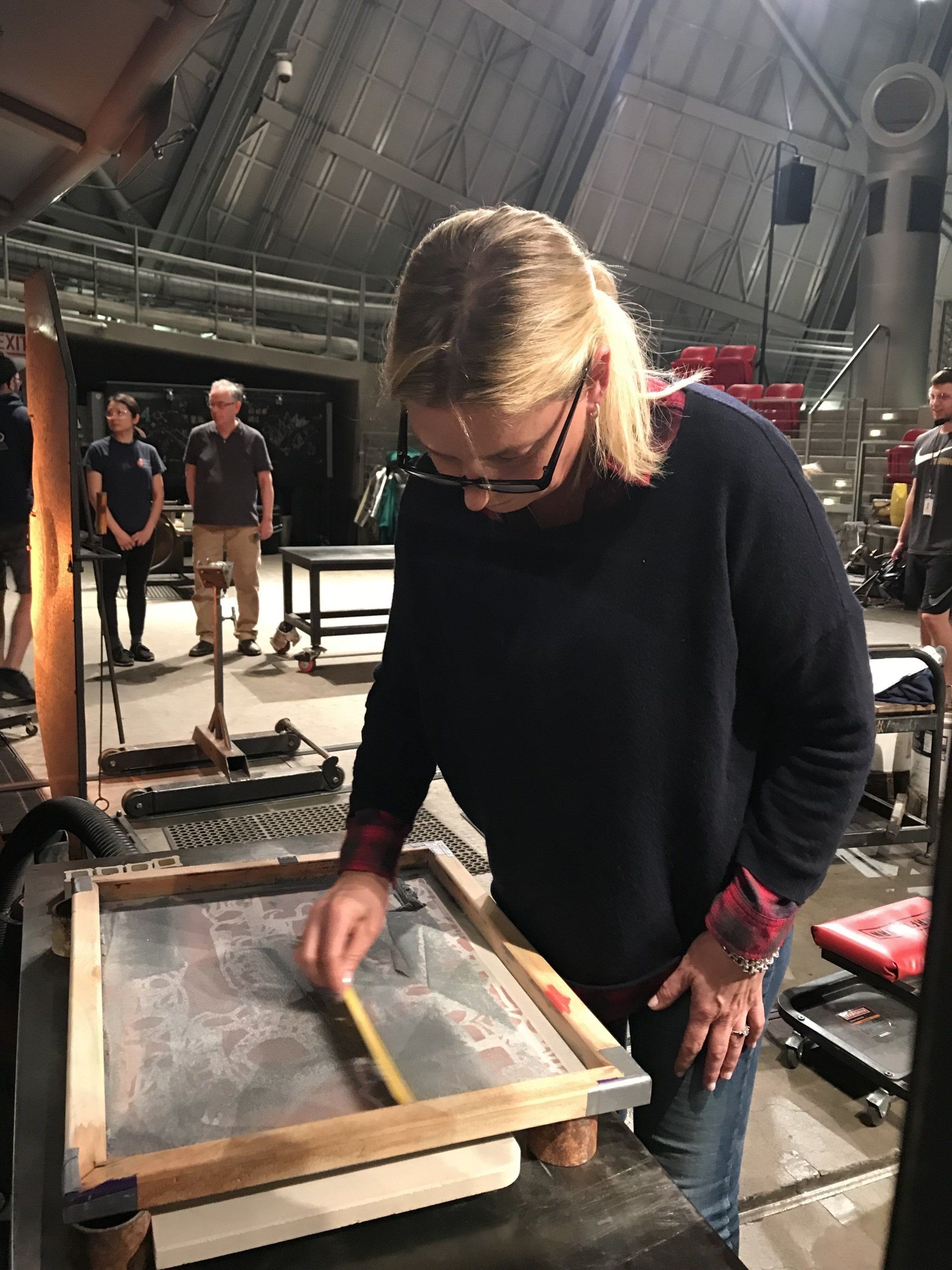 A woman in a black sweater is working on a screen printing machine