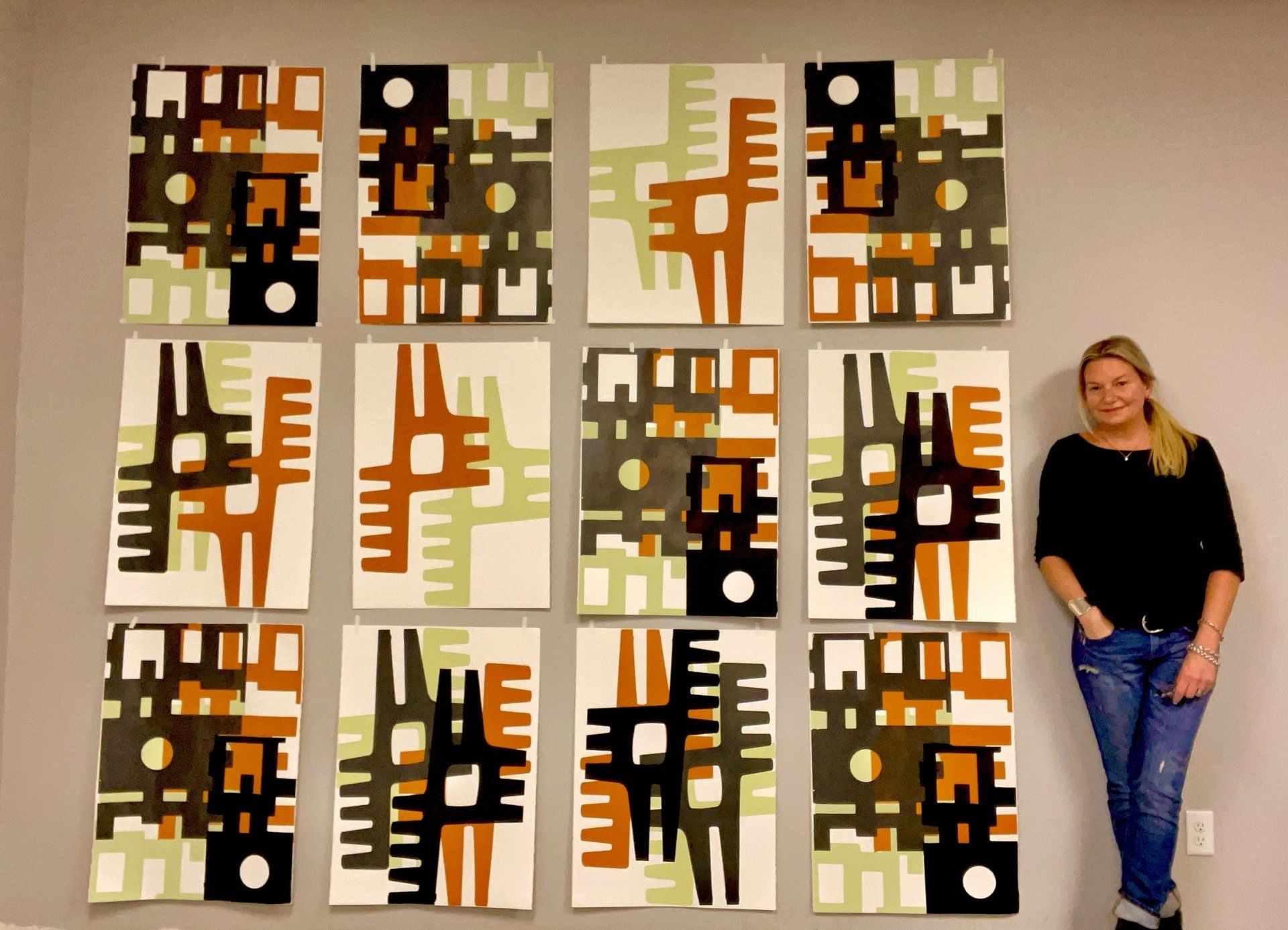A woman stands in front of a wall of paintings